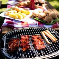 Close up of barbecue with buns and corn on table in park